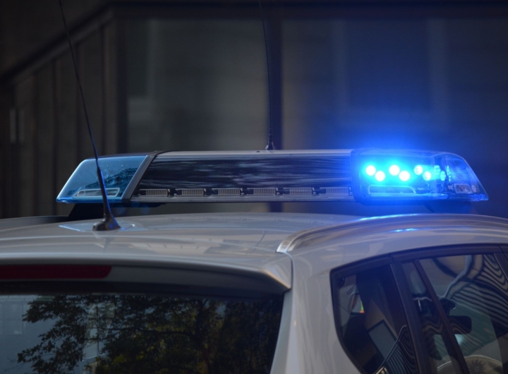Agenti di polizia in divisa eseguono un arresto, con auto della polizia sullo sfondo.