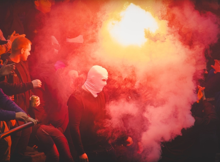 Immagine di tifosi in uno stadio durante una partita di calcio, con le forze dell'ordine presenti.