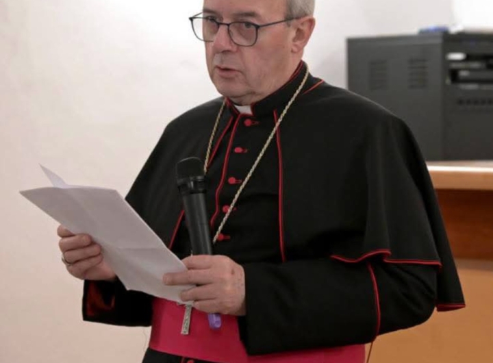 L'arcivescovo Franco Moscone, con abito talare, parla di fronte a un microfono.